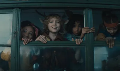 Crianças híbridas de Sweet Tooth sorridentes dentro de um veículo grande olhando para fora pela janela.