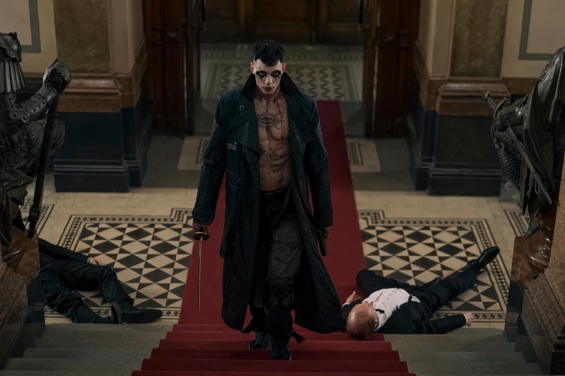 Personagem de O Corvo subindo uma escada com tapete vermelho e espada na mão.
