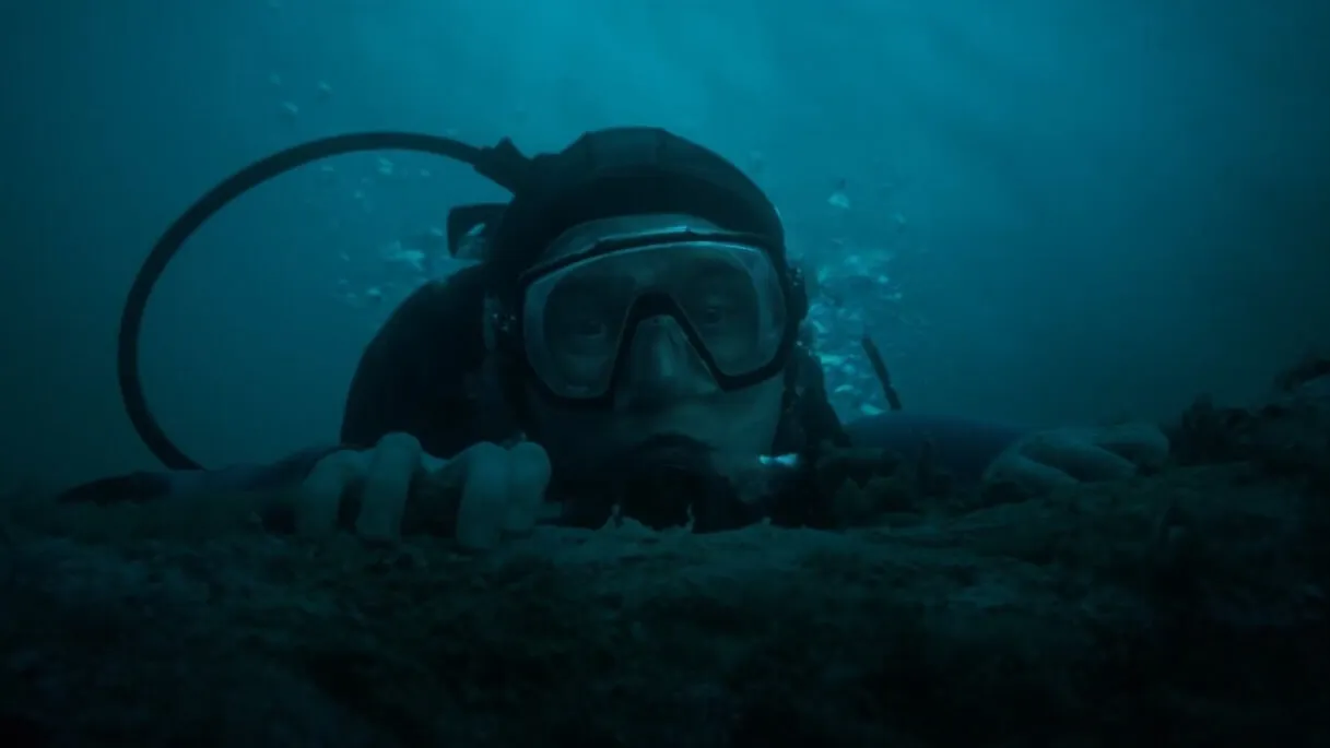 Homem com traje de mergulho no fundo do mar olhando para a frente