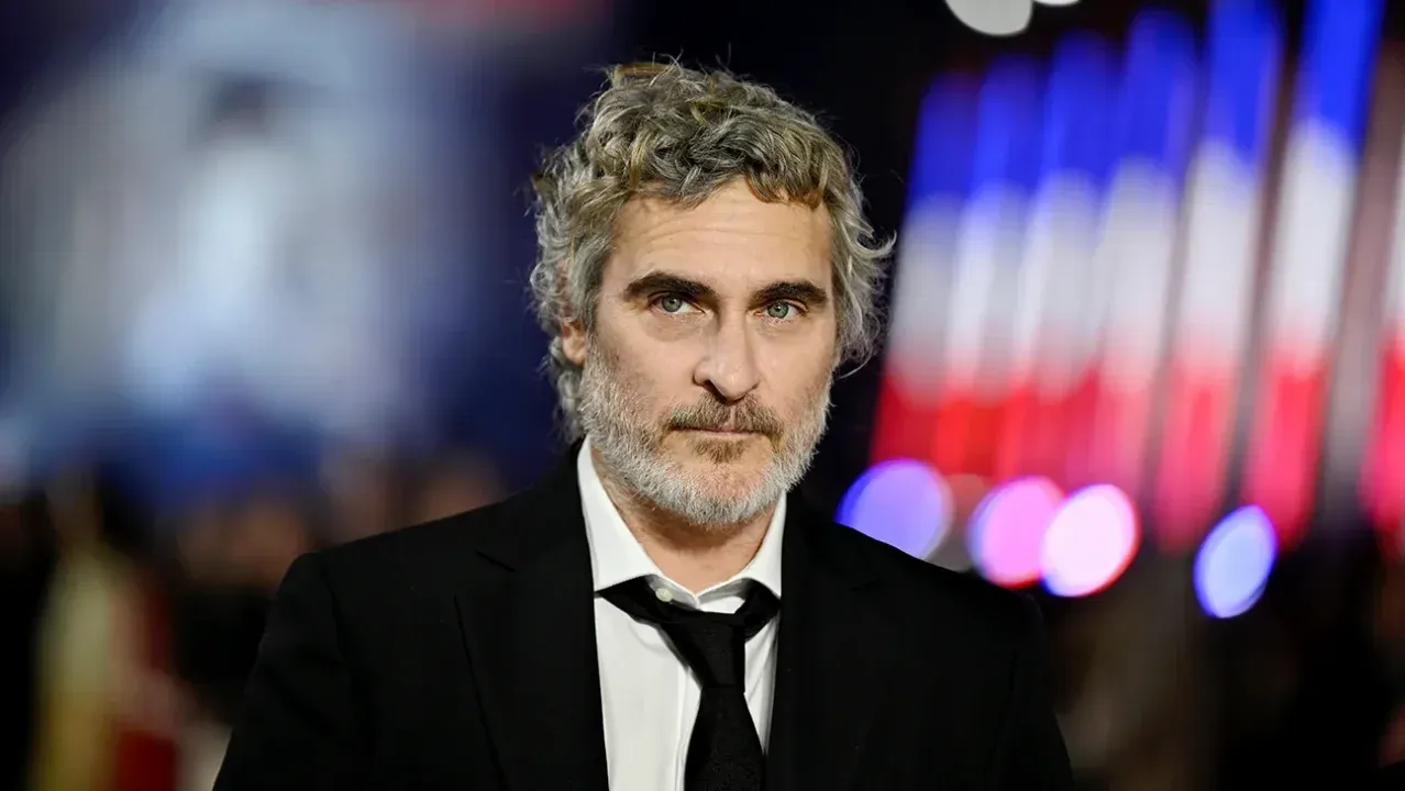 Joaquin Phoenix não olha diretamente para a câmera, usando terno e gravata.