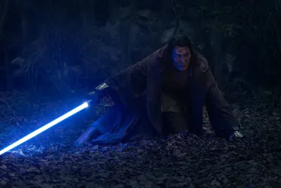 Homem caído no chão empunhando um sabre de luz azul, de Star Wars.