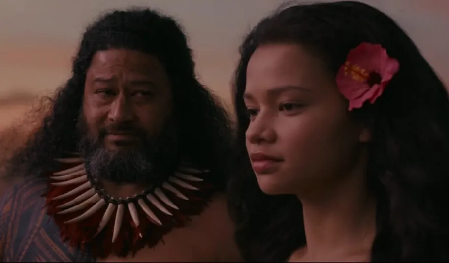 Mulher com flor vermelha no cabelo olhando para frrente enquanto homem olha para ela