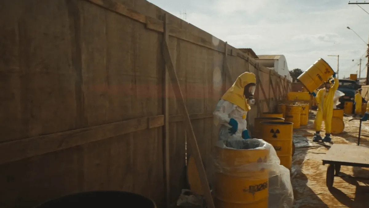 pessoas equipadas com roupa anti radiação levando latas grandes amarelas