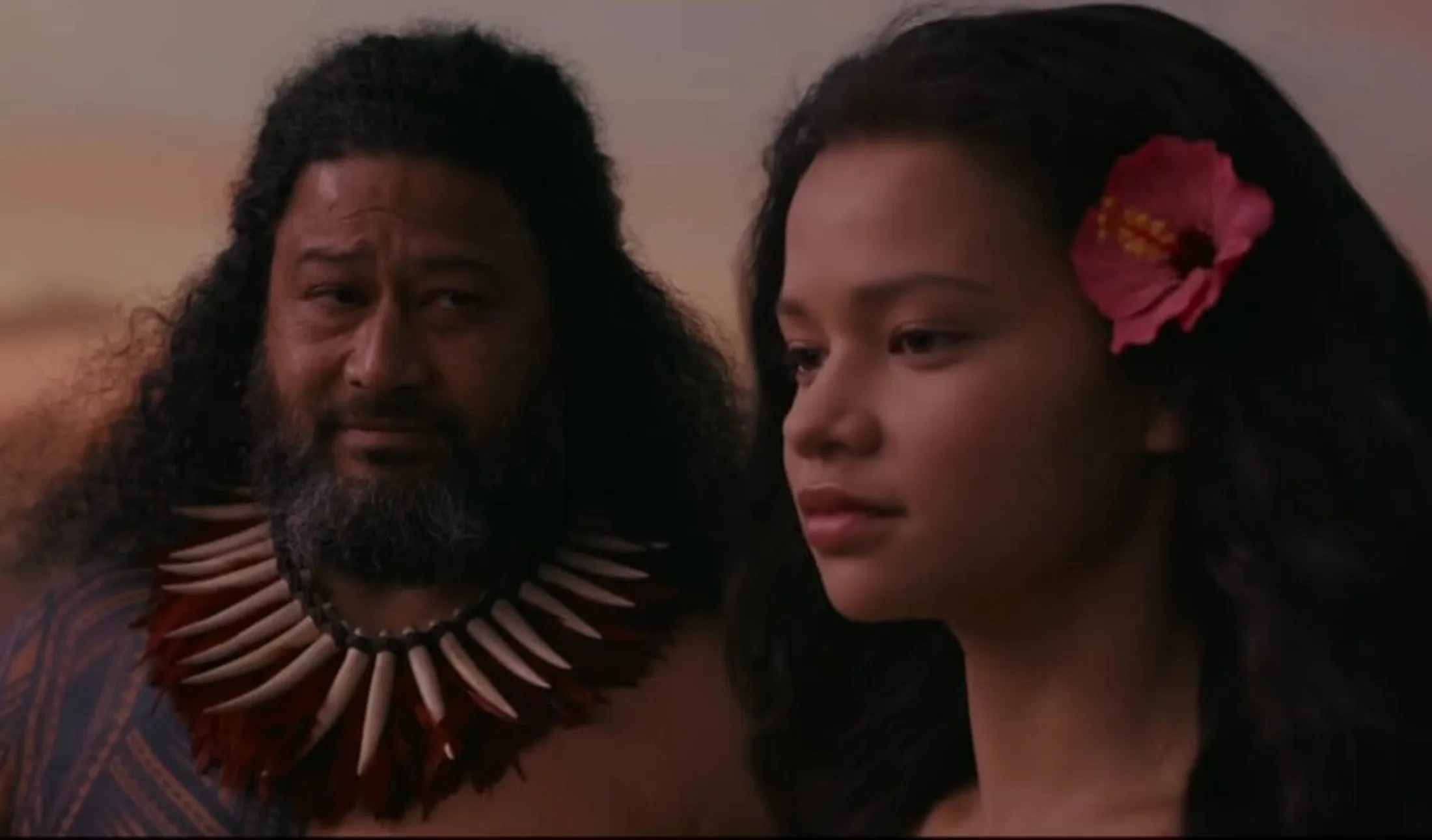 Mulher com flor vermelha no cabelo olhando para frrente enquanto homem olha para ela