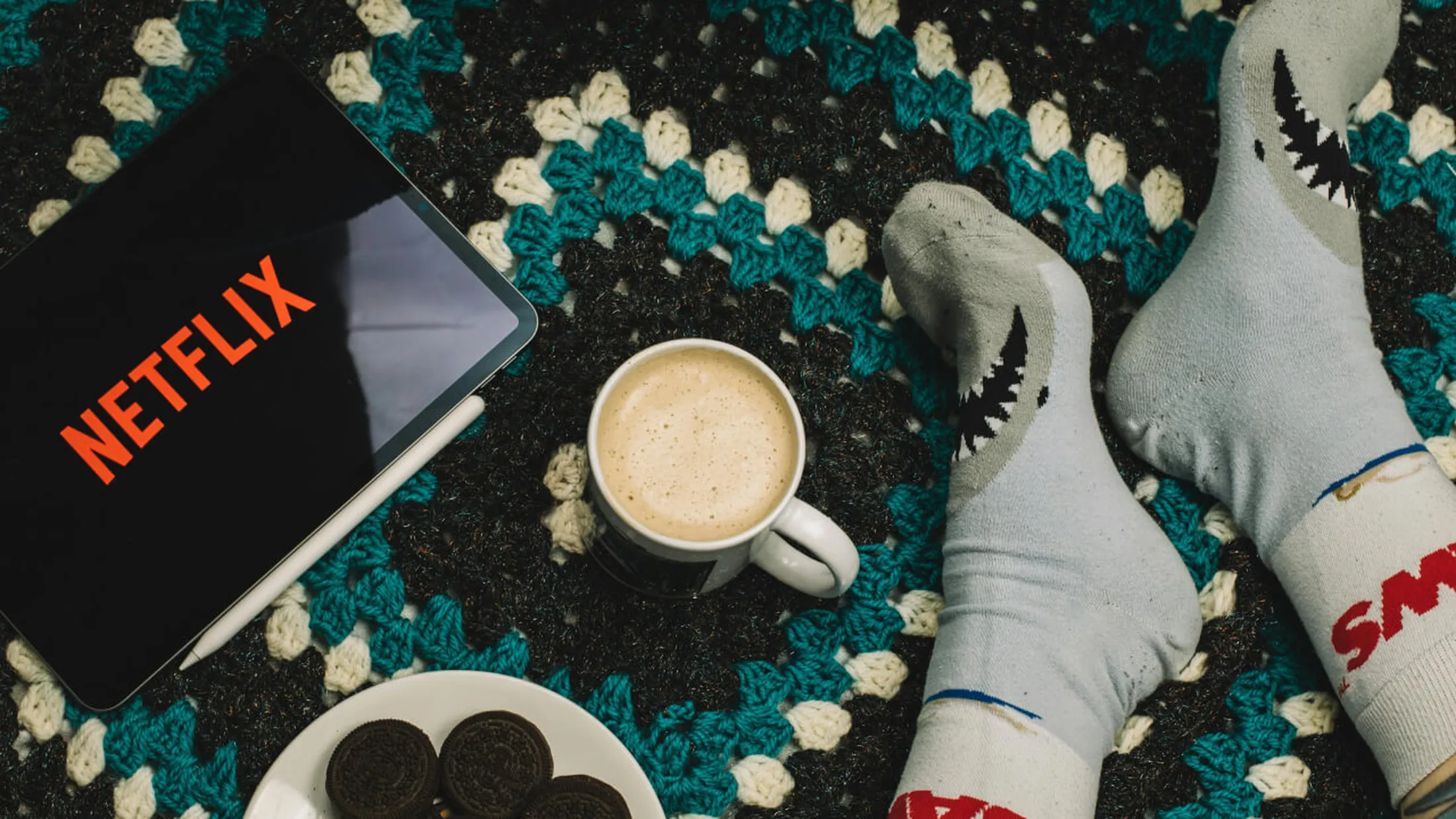 tablet com o logo da netflix, uma caneca com café e um prato com biscoitos