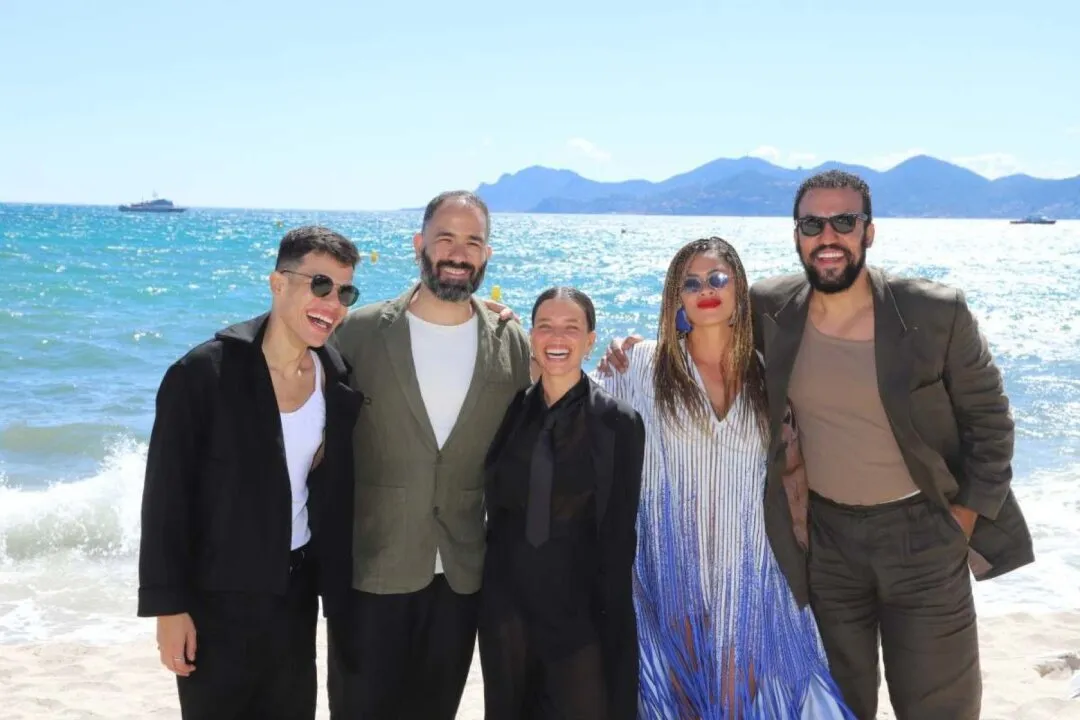 Elenco de filme brasileiro enfileirado com roupas de gala. Ao fundo, o mar de Cannes.