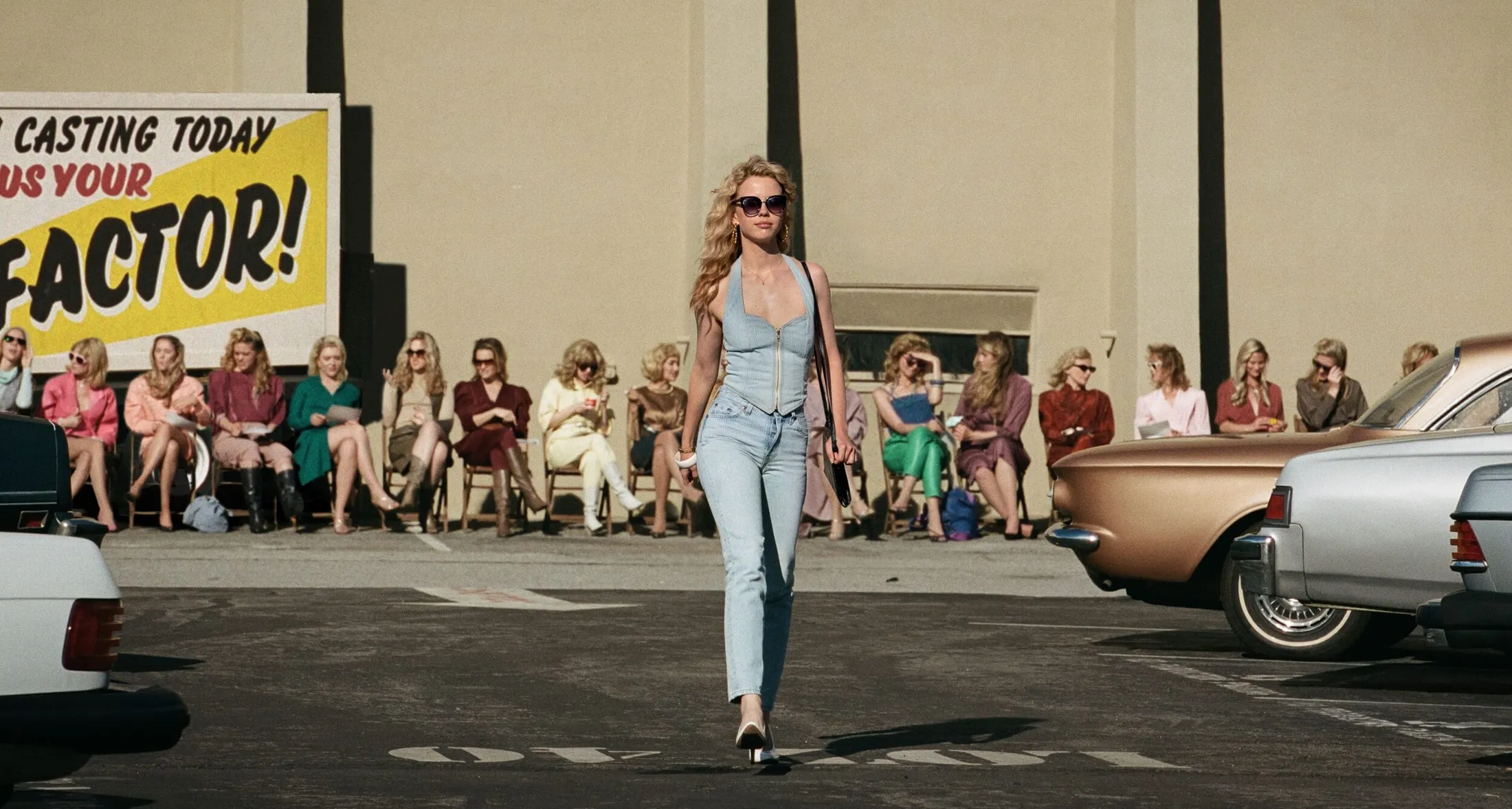 Personagem de MaXXXine desfilando de roupa jeans com óculos de sol e salto alto.