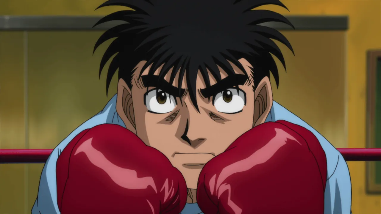 Ippo vestido de uma camisa azul clara básica, sério e em posição de guarda, com suas luvas de boxe.