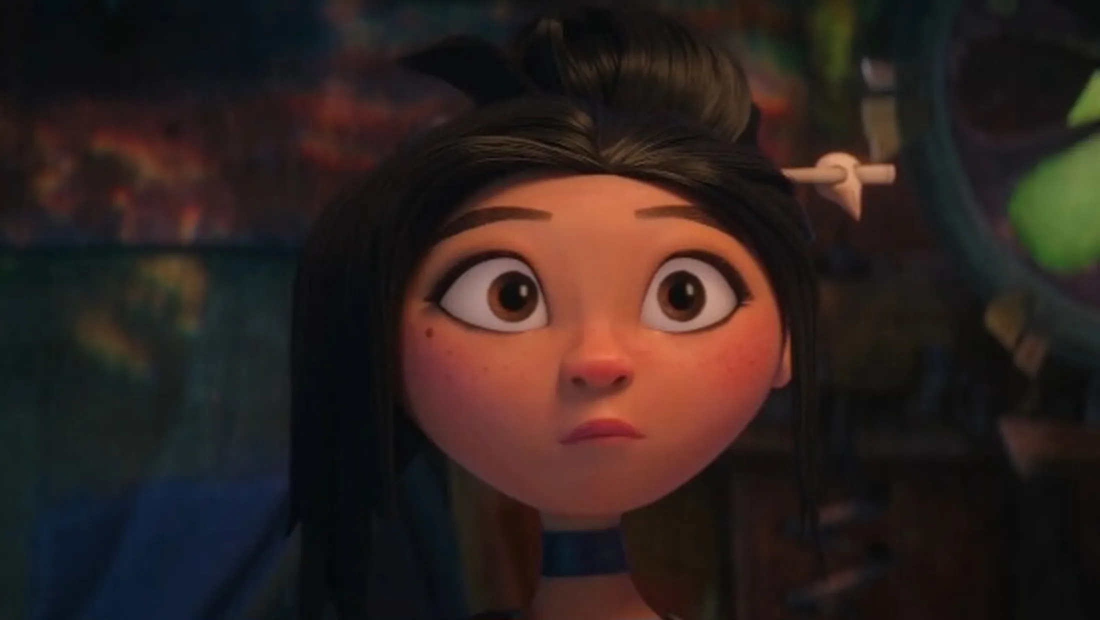 Menina de cabelos pretos presos e de franja olhando surpresa para a frente usando um colar