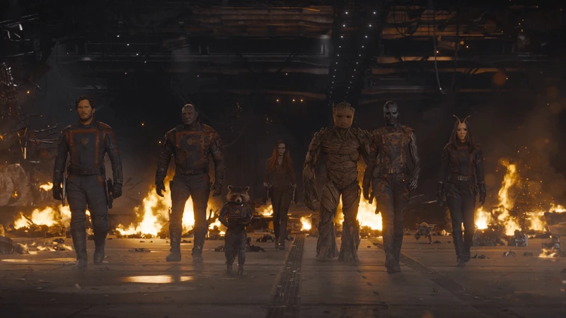 Imagem mostrando Peter Quill, Drax, Rocket, Gamora, Groot, Nebulosa e Mantis, com um fogo atrás mostrando uma explosão