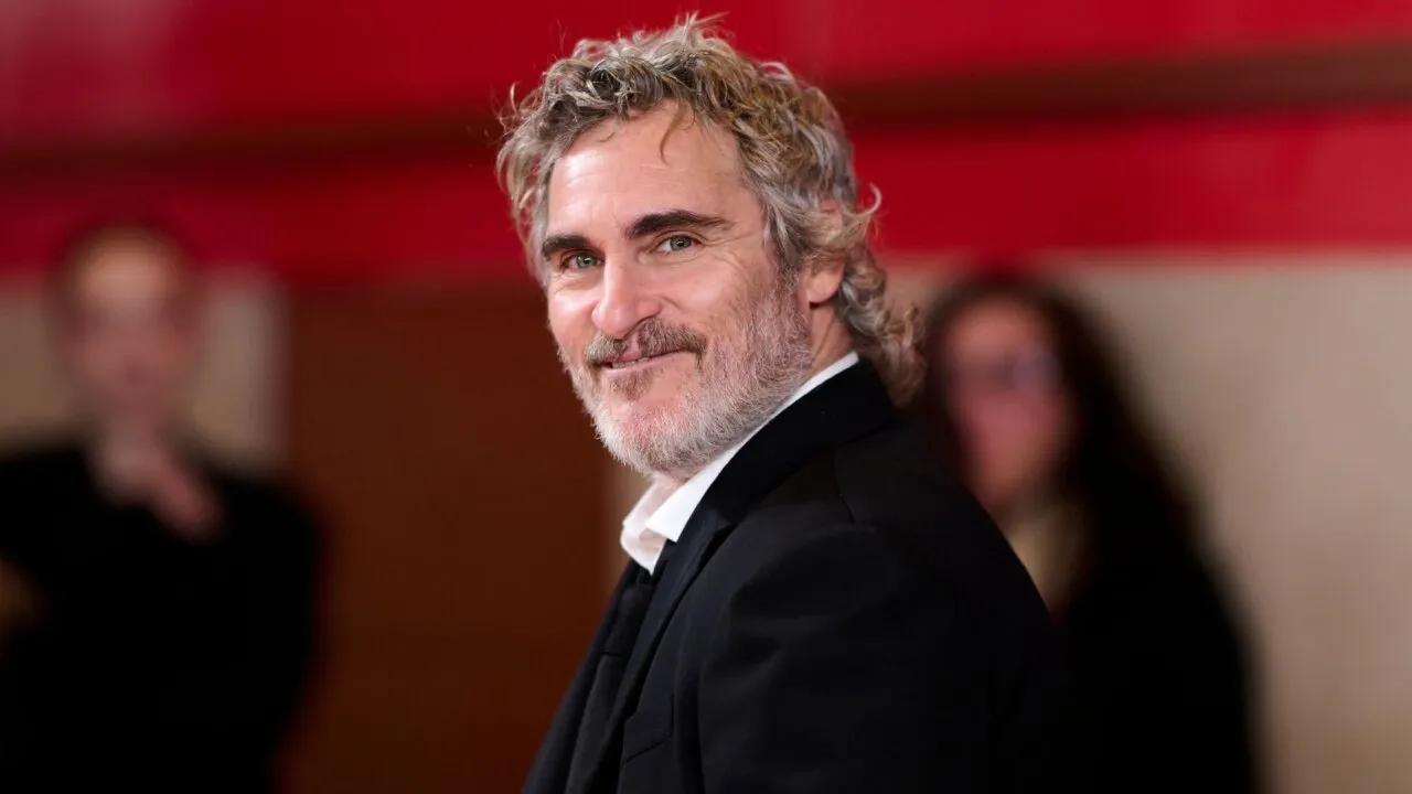 Joaquin Phoenix sorrindo, com barba grisalha por fazer e vestindo traje de gala.